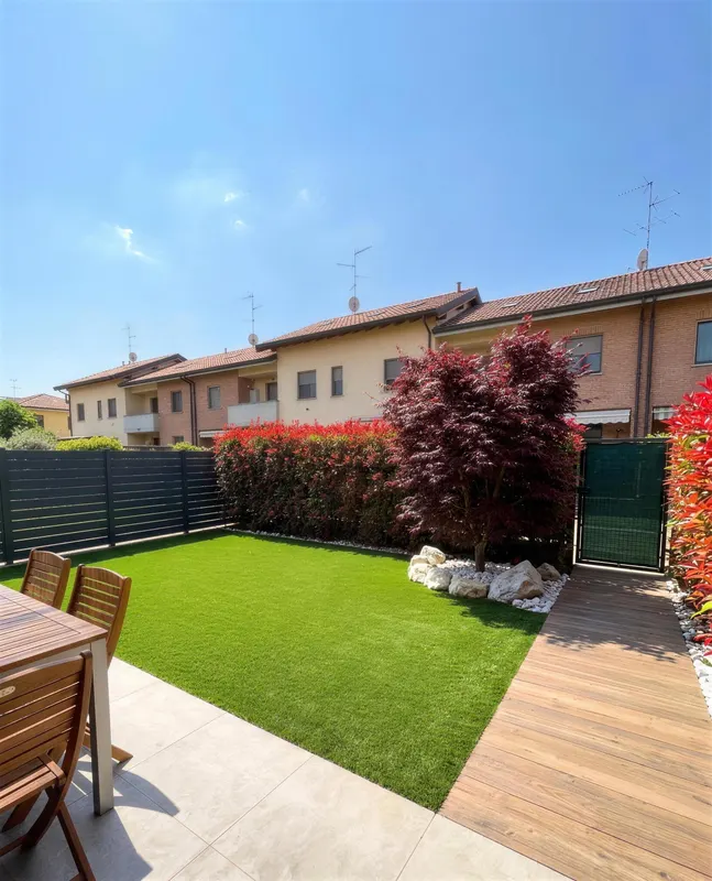 Giardino di 100 m² a Monza con camminamento in legno che arriva al cancello, sassi bianchi che tengono pulito il bordo