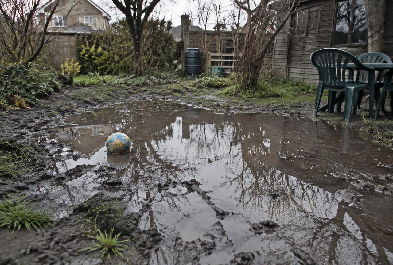 Giardino allagato e pieno di fango dopo la pioggia, con un pallone nella pozzanghera